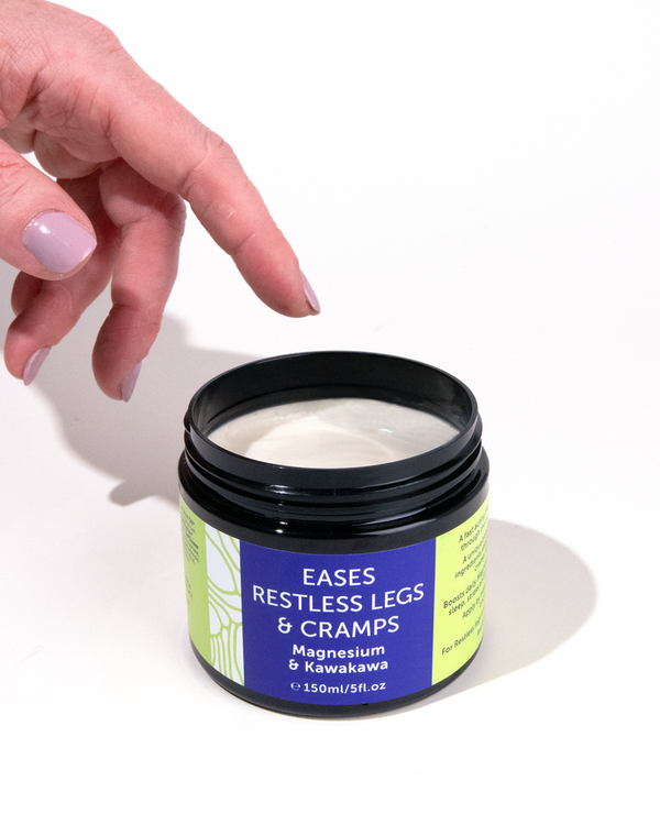 A hand reaching into an open tub of Magnesium and Kawakawa Cream.