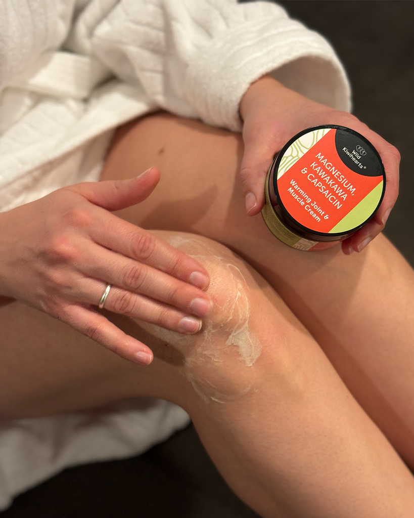 A woman rubbing some Wild Kiwihearts Magnesium, Kawakawa & Capsaicin cream on her knee